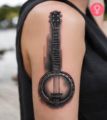 A black and gray shaded banjo tattoo on the upper arm