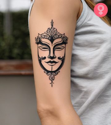A minimalist drama mask tattoo on the upper arm