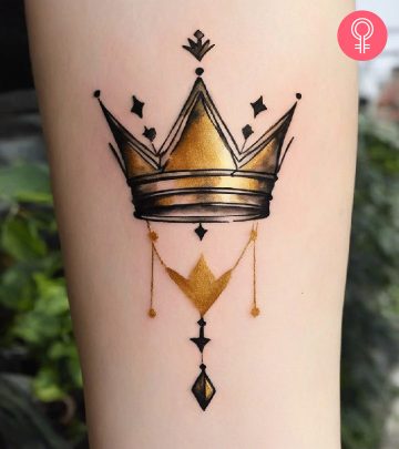 A minimalist watercolor golden crown tattoo on the arm