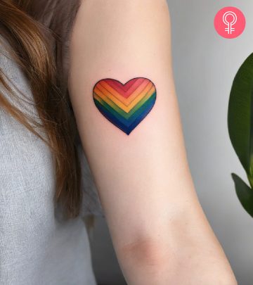 A rainbow-colored heart tattoo on the inner upper arm of a woman