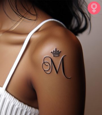 A woman wearing a M letter tattoo with a crown on the upper arm