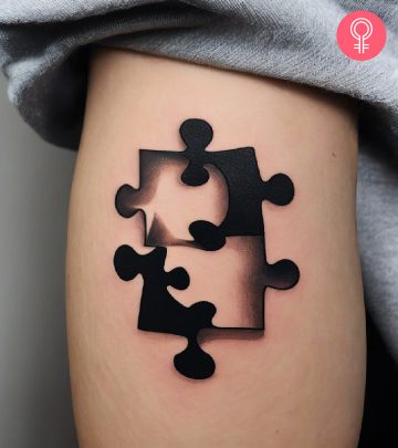 A black and white puzzle piece tattoo on the upper arm of a woman