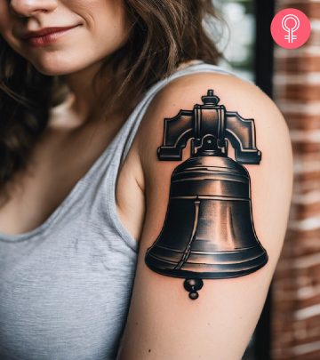 Liberty bell tattoo on the upper arm of a woman