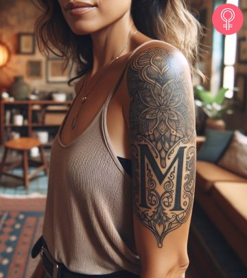 M tattoo with floral patterns on the upper arm