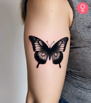 A black butterfly tattoo on the upper arm